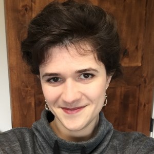 Picture is a headshot of Alexis. Her dark brown hair is back in a loose bun, and she is looking at the camera with a close-mouthed smile.